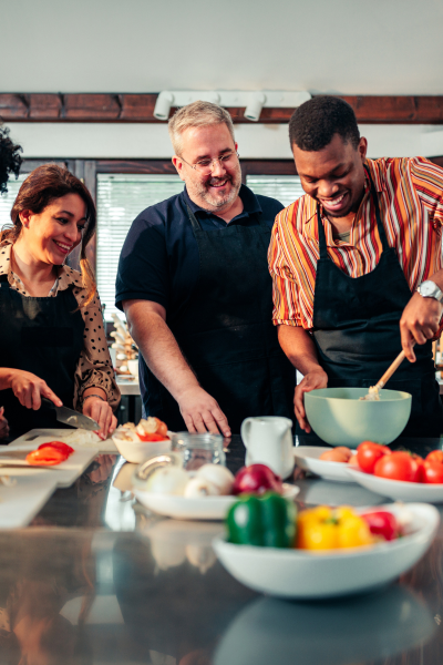 group cooking class with male teacher in the centre and a young man stirring something while a woman looks on
